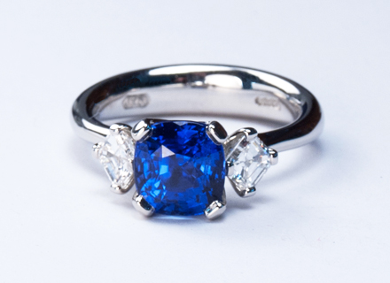Four claw three stone platinum ring with a cushion cut blue sapphire and diamonds